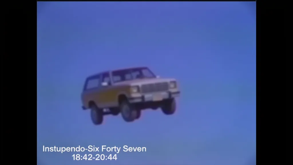 cartoon A vintage-style video still showing a car floating in a clear blue sky. The vehicle resembles an older model SUV or truck. Text at the bottom reads "Instupendo-Six Forty Seven 18:42-20:44," indicating a timestamp or track title. The image appears to capture a surreal or edited scene.